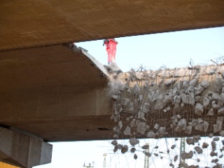 Der Presslufthammer am Bagger schlägt ganze Betonbrocken aus der Brücke, die dann zu Boden fallen.